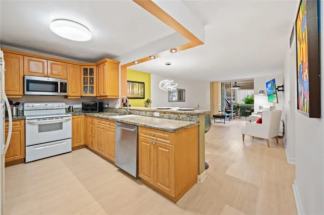 a kitchen with stainless steel appliances granite countertop a stove top oven a sink dishwasher and a refrigerator with wooden floor