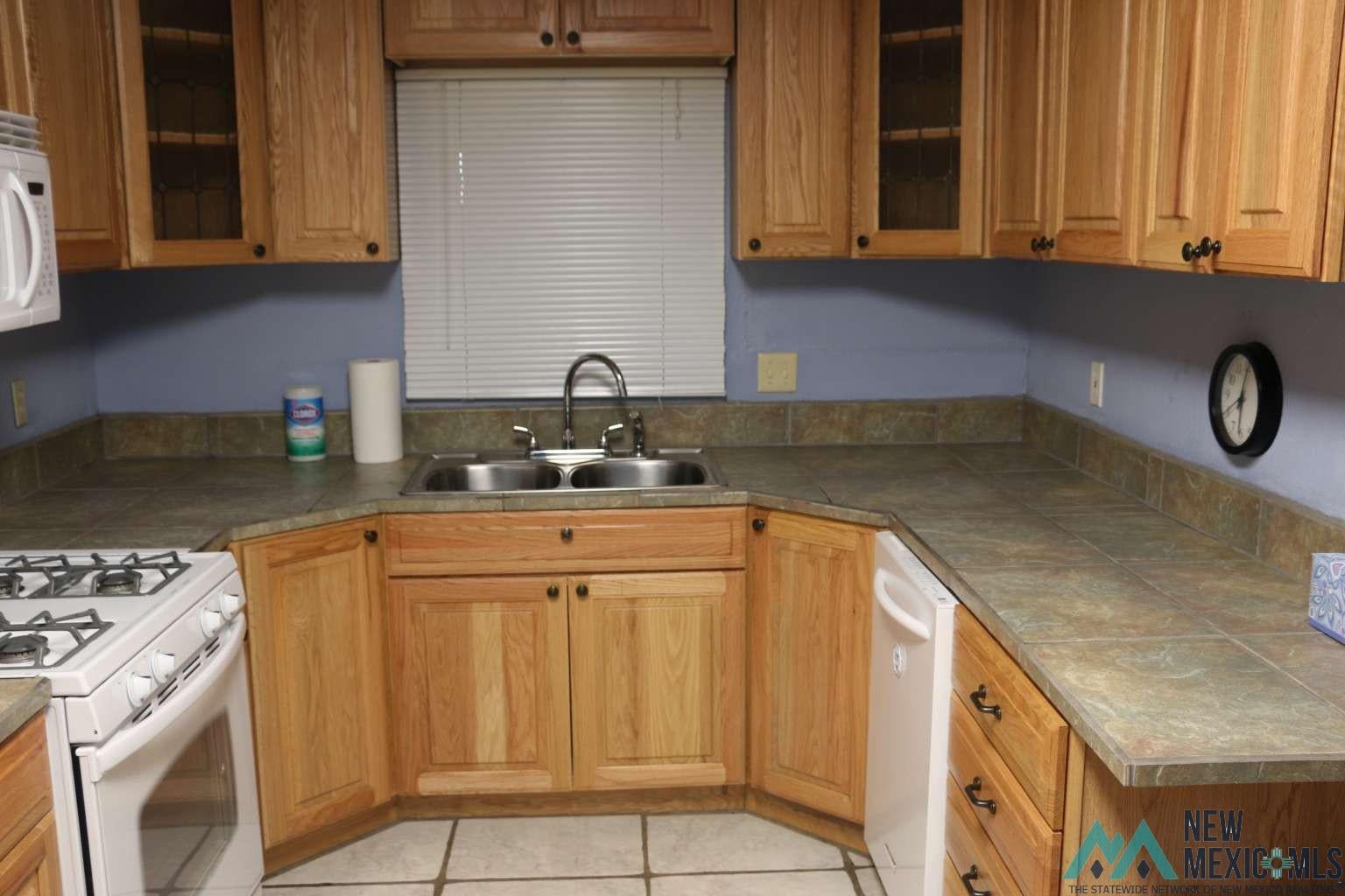 32 Dan Gatlin Road Pie Town, NM 87827 - Photo 6 of 43 Kitchen featuring glass insert cabinets, white appliances, brown cabinetry, light tile patterned floors, and tile countertops