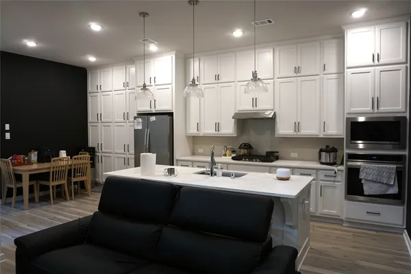 a kitchen with stainless steel appliances kitchen island granite countertop a dining table chairs refrigerator and microwave