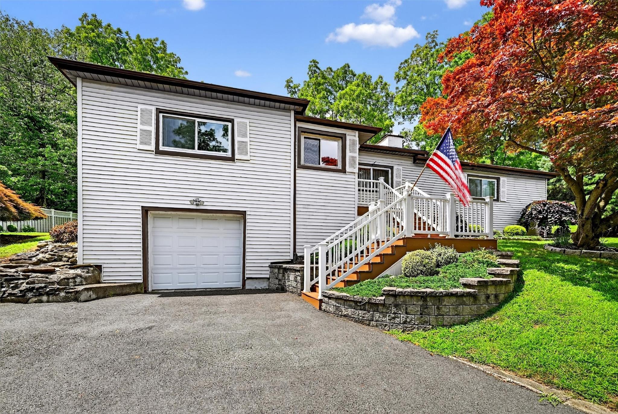 View of front of property with a garage, asphalt driveway, a trex deck, stairs, and a front lawn
