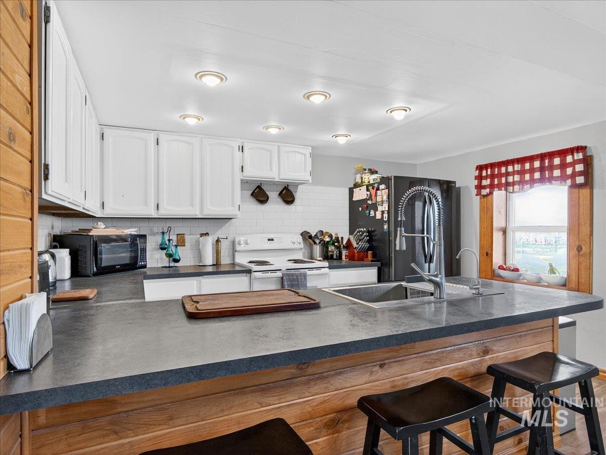 2588 West Sales Yard Road Emmett, ID 83617 - Photo 20 of 50 Kitchen featuring dark countertops, white range with electric stovetop, a breakfast bar area, and freestanding refrigerator