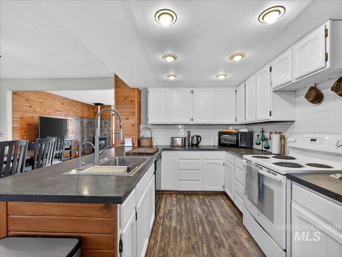 2588 West Sales Yard Road Emmett, ID 83617 - Photo 21 of 50 Kitchen with dark countertops, white range with electric cooktop, white cabinets, wood walls, and dark wood-style floors