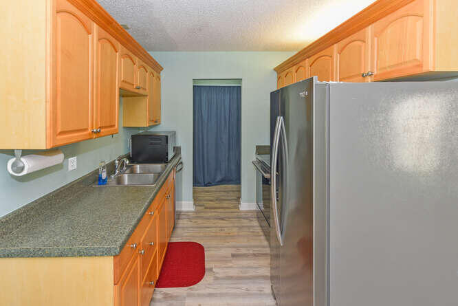 150 Pineview Road, Unit L6 Jupiter, FL 33469 - Photo 12 of 31 a kitchen with stainless steel appliances granite countertop a refrigerator a stove and a sink with wooden floor