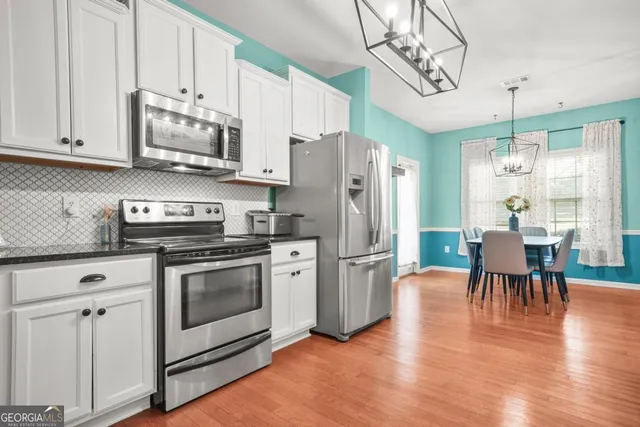 a kitchen with stainless steel appliances granite countertop a stove a refrigerator a microwave oven a dining table and chairs with wooden floor