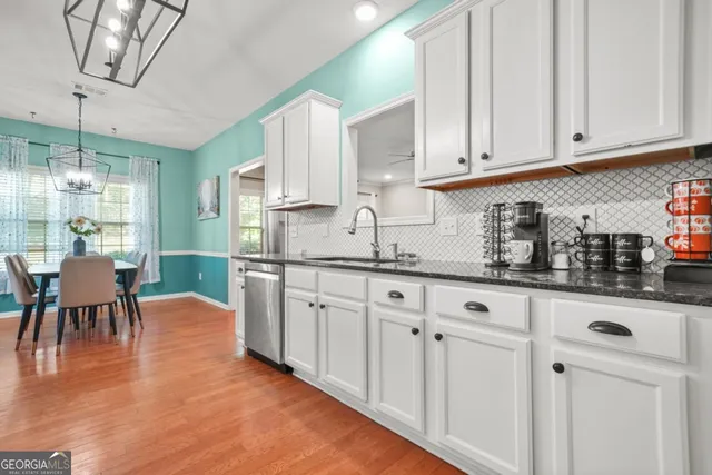 a kitchen with stainless steel appliances granite countertop a stove a sink dishwasher and white cabinets with wooden floor