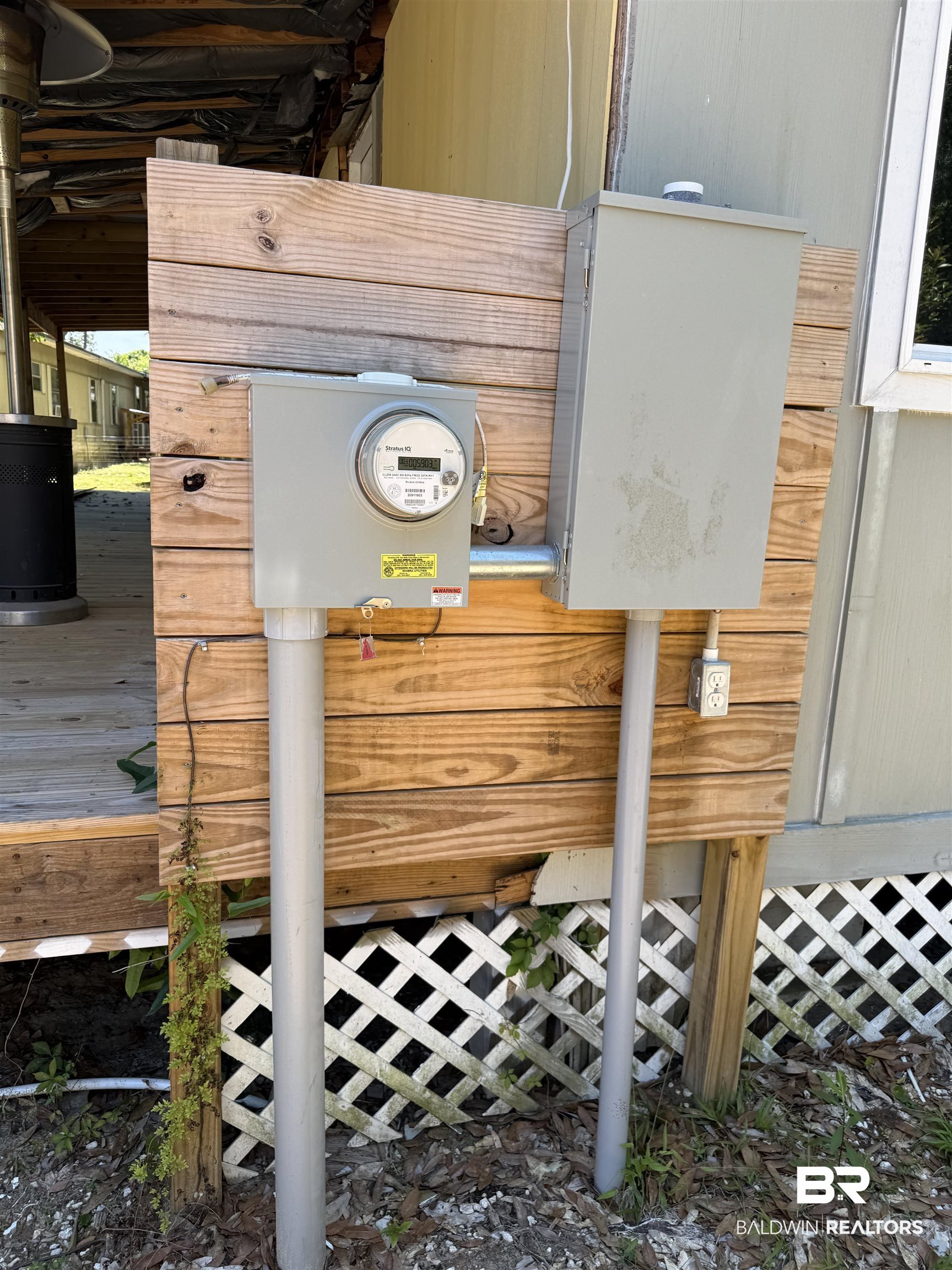 1276 Rio Circle Lillian, AL 36549 - Photo 7 of 7 Exterior utility meters and electrical panels featuring a wood-slat privacy screen and white lattice skirting
