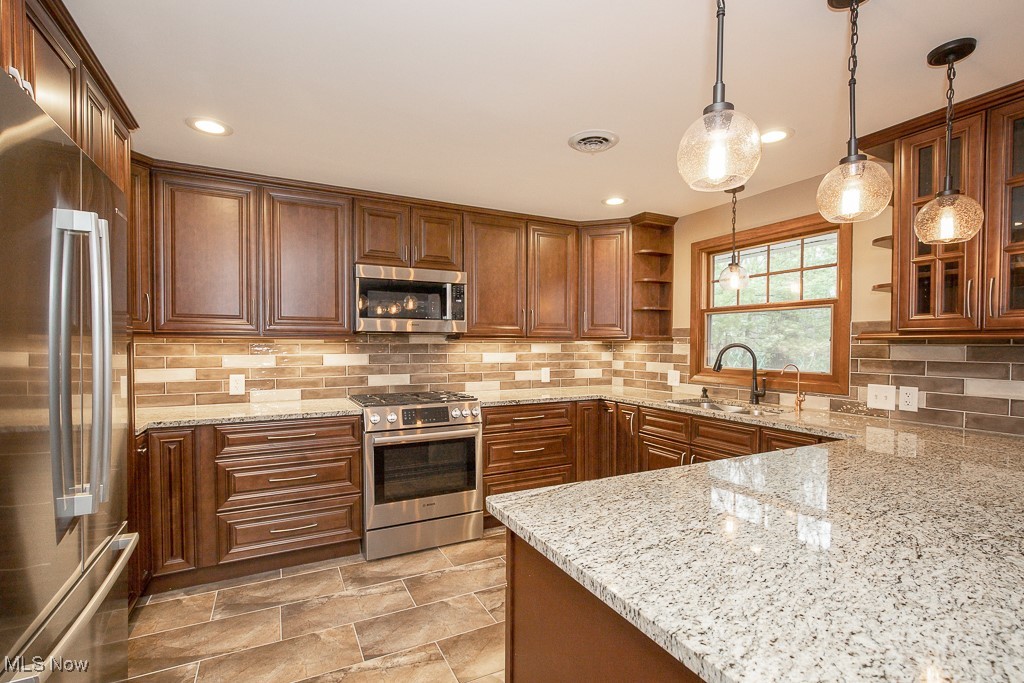 2969 Center Road Avon, OH 44011 - Photo 9 of 33 Kitchen featuring pendant lighting, backsplash, sink, light stone countertops, and stainless steel appliances