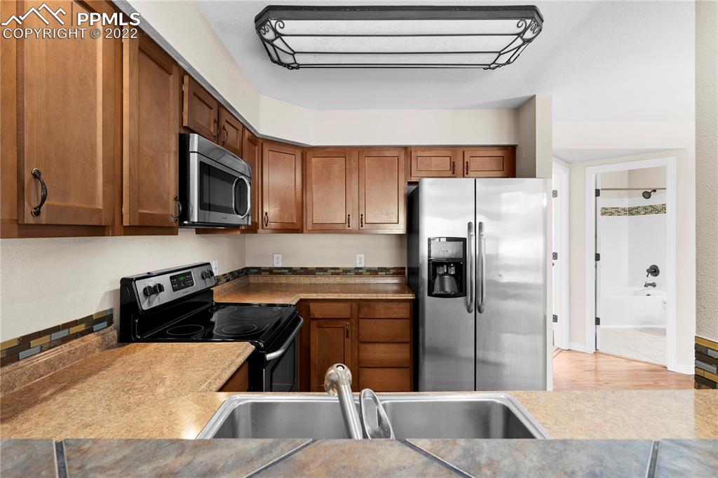 6910 Los Reyes Circle Colorado Springs, CO 80918 - Photo 5 of 38 a kitchen with stainless steel appliances granite countertop a refrigerator a stove and a sink with wooden cabinets