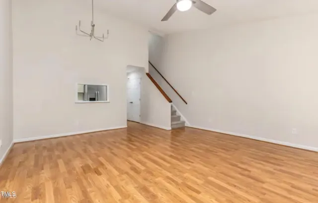 a view of an empty room with wooden floor and a ceiling fan