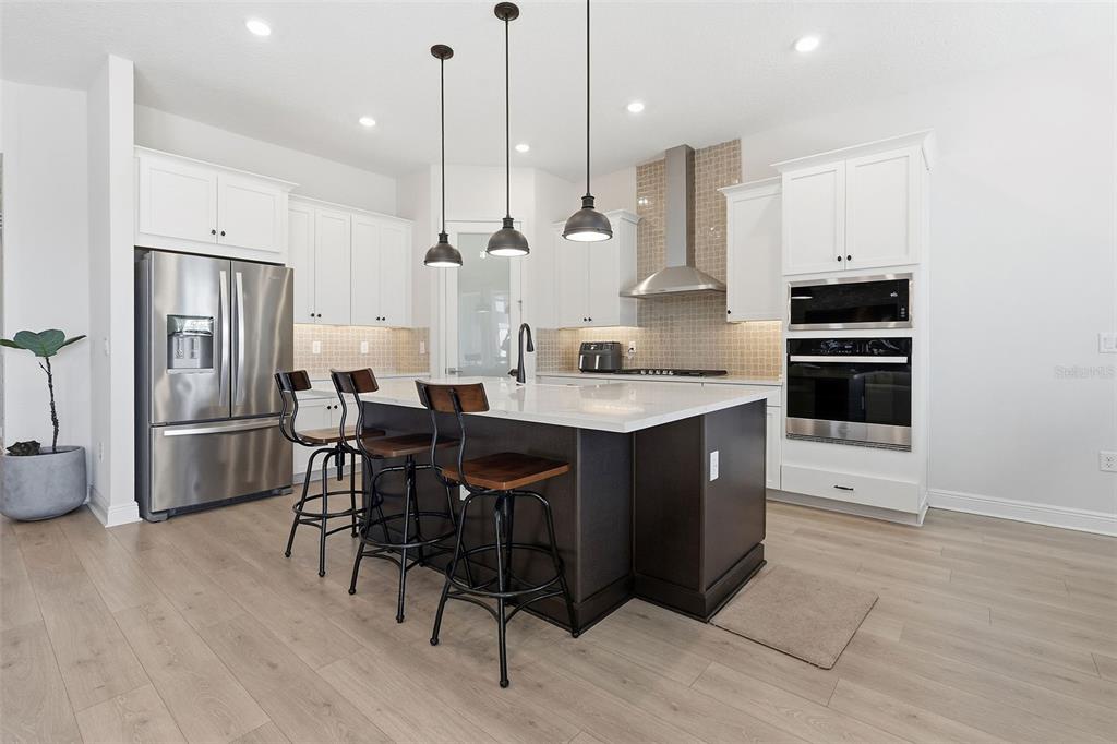 16131 Volterra Point Bella Collina, FL 34756 - Photo 20 of 52 a kitchen with stainless steel appliances kitchen island granite countertop a refrigerator a stove a sink a dining table and chairs with wooden floor