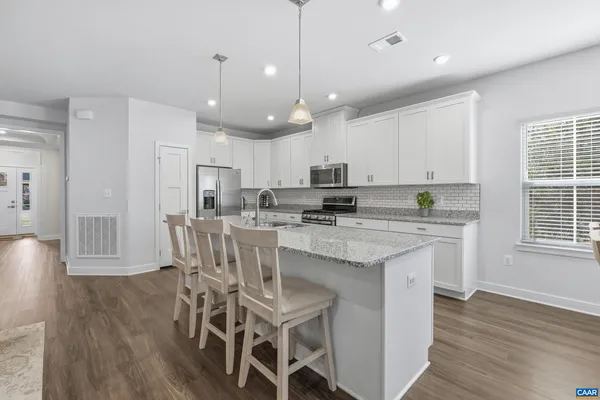 a kitchen with stainless steel appliances granite countertop a stove top oven a refrigerator a sink and chairs