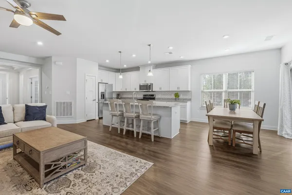 a living room with stainless steel appliances furniture wooden floor and a kitchen view