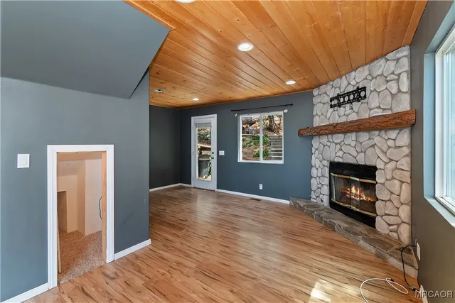 a view of an empty room with wooden floor a fireplace and a window