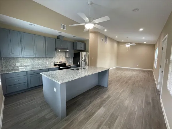 a large kitchen with stainless steel appliances a large counter top a sink dishwasher and a stove with wooden floors