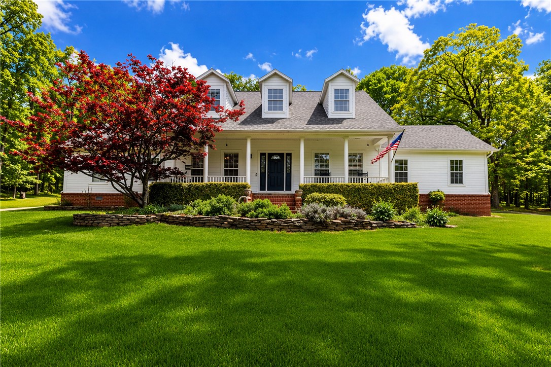 14203 Greenridge Road Fayetteville, AR 72701 - Photo 1 of 25 White siding residence featuring a covered front porch with white columns and railings, dormer windows, and a red brick foundation. This image is altered by AI to show green grass.