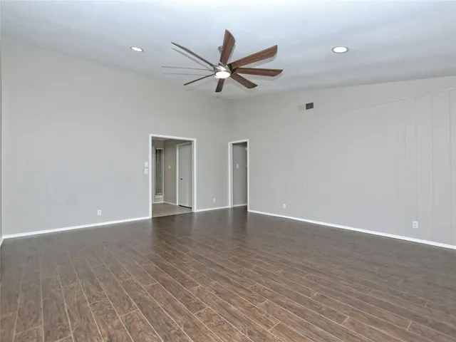 a view of an empty room with wooden floor and a ceiling fan