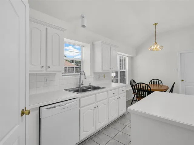 a kitchen with a sink dishwasher and white cabinets with wooden floor