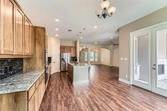 a view of a kitchen with kitchen island granite countertop wooden floors wooden cabinets a counter top space and stainless steel appliances