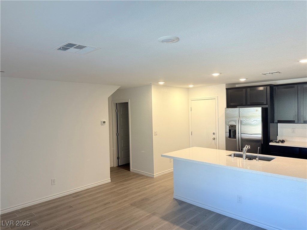 10772 Astell Isle Court Las Vegas, NV 89166 - Photo 3 of 32 Kitchen featuring dark cabinetry, stainless steel fridge, light stone counters, light wood-type flooring, and recessed lighting