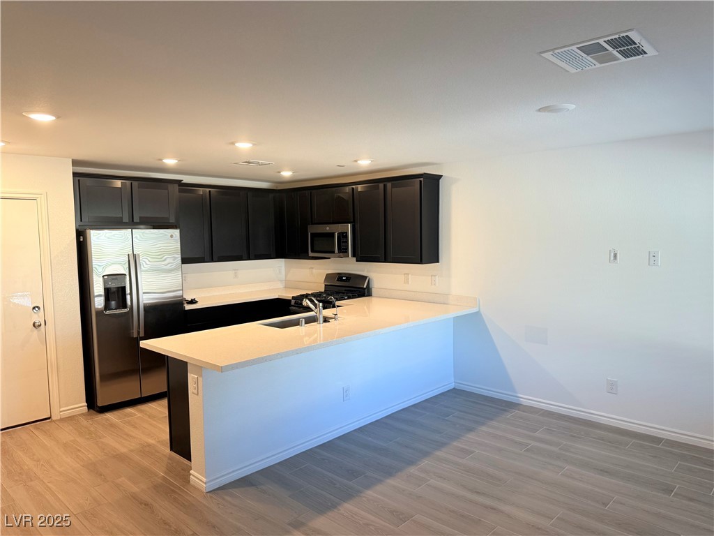 10772 Astell Isle Court Las Vegas, NV 89166 - Photo 4 of 32 Kitchen with dark cabinets, stainless steel appliances, a peninsula, light wood-style flooring, and recessed lighting