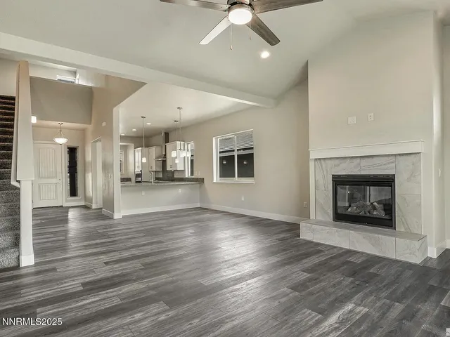 an empty room with wooden floor fire place and kitchen view