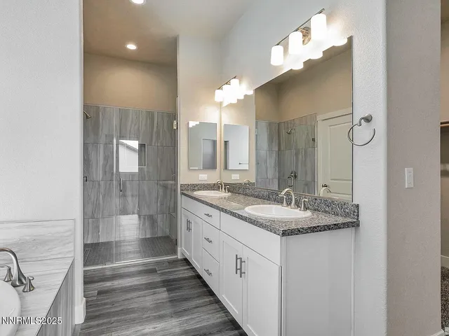 a bathroom with a granite countertop double vanity sink a mirror and a shower