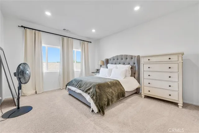 a spacious bedroom with a bed a dresser and a large window