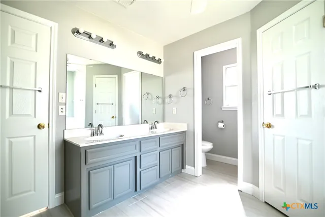a spacious bathroom with a double vanity sink a toilet and a mirror