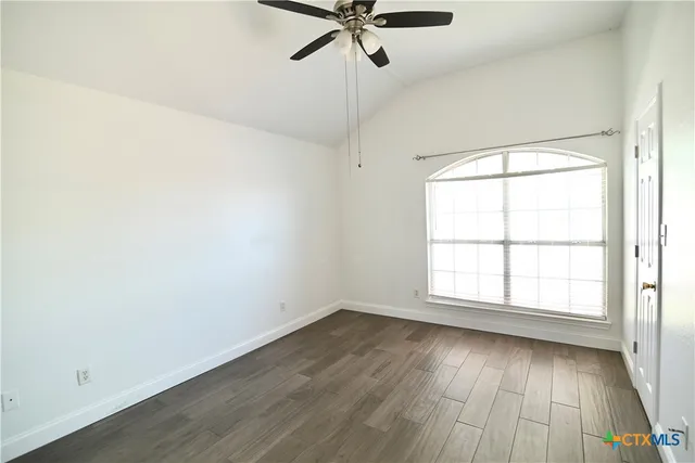 an empty room with wooden floor fan and windows