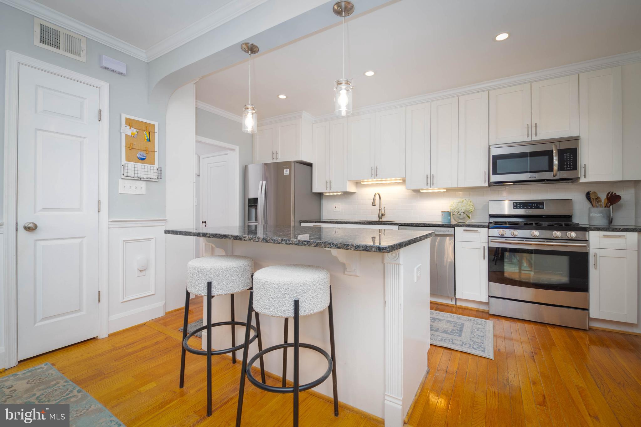 409 Regester Avenue Baltimore, MD 21212 - Photo 16 of 44 a kitchen with stainless steel appliances granite countertop a stove a sink a microwave a refrigerator and white cabinets with wooden floor