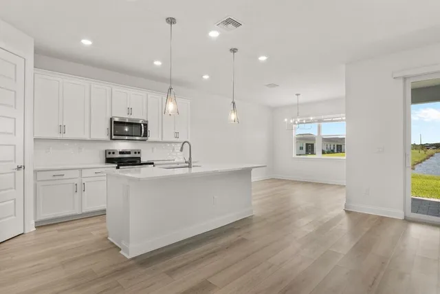 a kitchen with stainless steel appliances granite countertop a refrigerator a sink dishwasher a oven and a dining table with wooden floor