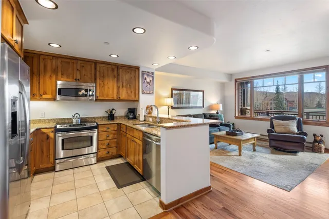 a kitchen with stainless steel appliances granite countertop a stove top oven a sink a dining table and chairs with wooden floor