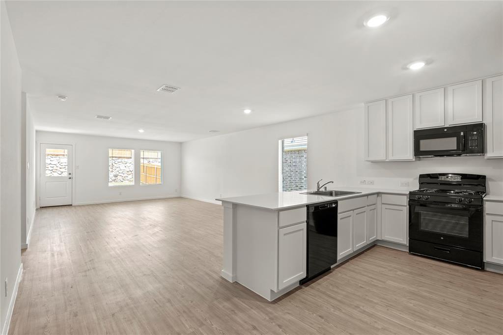 1138 Barbary Flds Street Forney, TX 75126 - Photo 4 of 25 Open-concept kitchen and living area featuring wood-finish flooring, white cabinetry, a kitchen island with sink, and black appliances