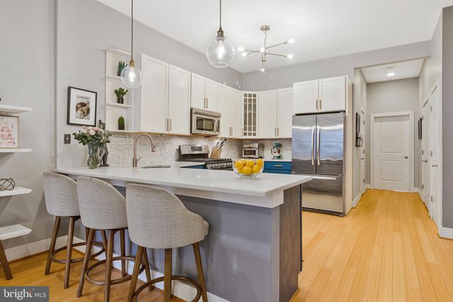 a kitchen with stainless steel appliances a refrigerator a stove a sink a dining table and chairs with wooden floor