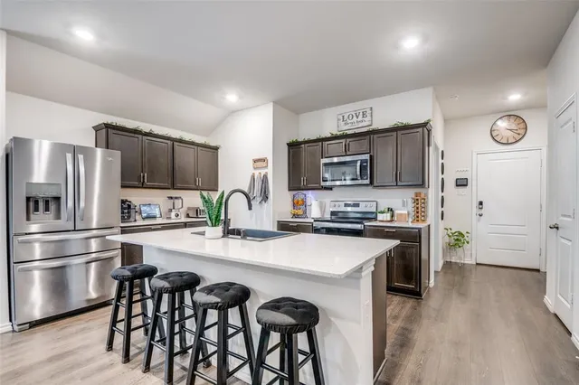 a kitchen with stainless steel appliances granite countertop a refrigerator a stove top oven a sink dishwasher and white cabinets with wooden floor