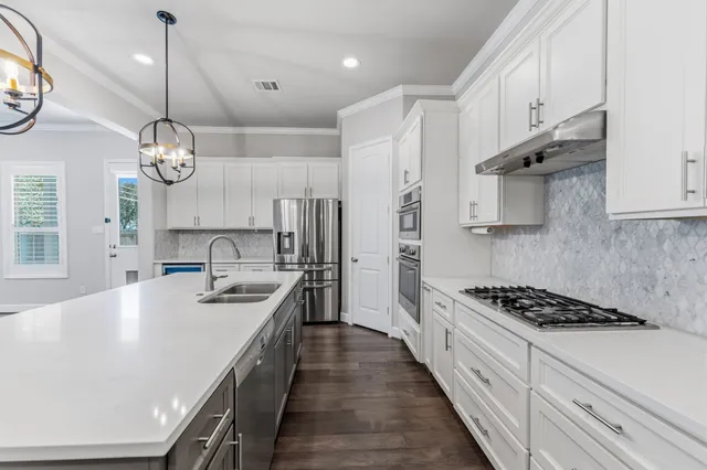 a kitchen with stainless steel appliances a stove a sink dishwasher and white cabinets with wooden floor