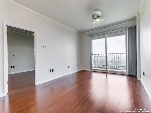 a view of an empty room with wooden floor and a window