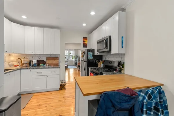 a kitchen with stainless steel appliances granite countertop a sink dishwasher a stove a microwave oven with white cabinets and wooden floor