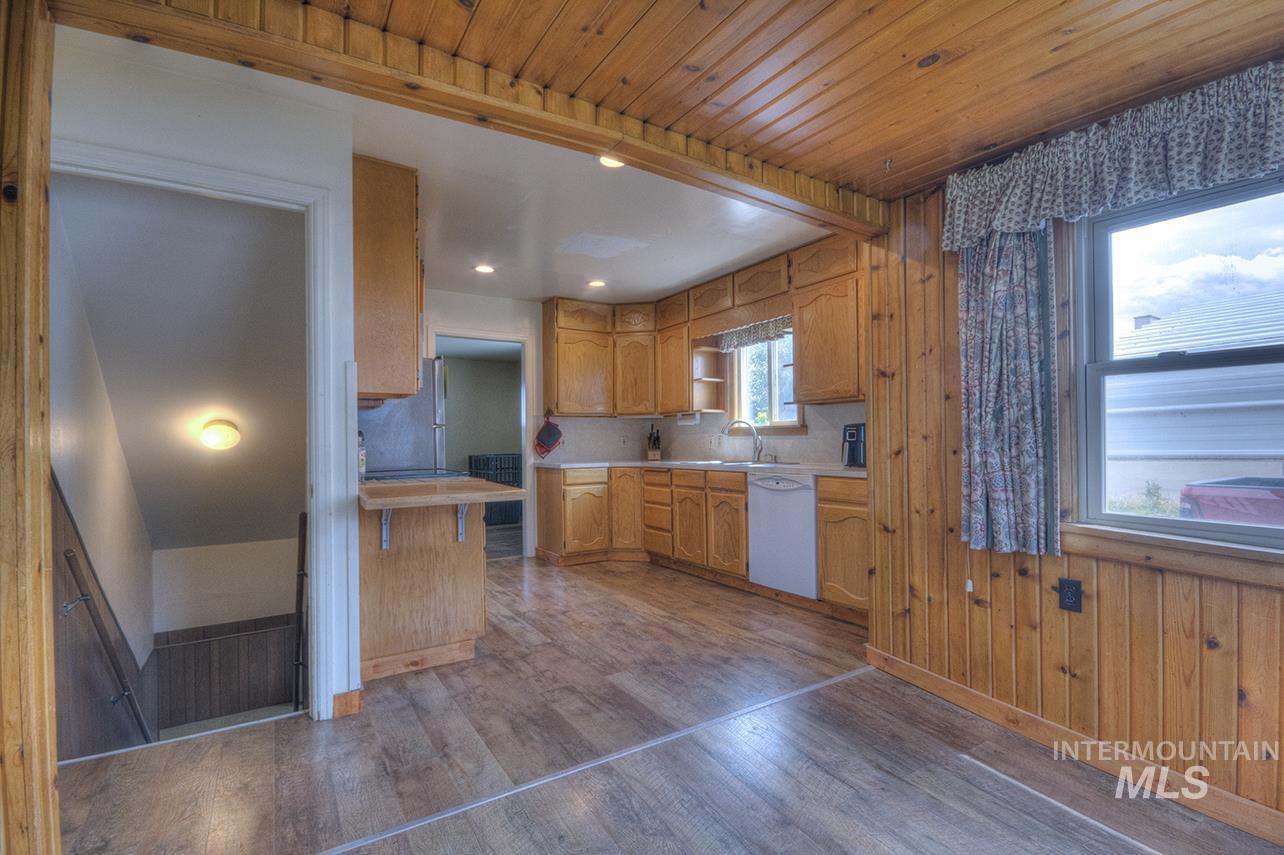 351 West Main Street South Vale, OR 97918 - Photo 17 of 33 Kitchen featuring wood-panel walls, wood-finish flooring, wood cabinetry, a white dishwasher, and a window above the sink