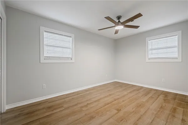 an empty room with wooden floor chandelier fan and windows