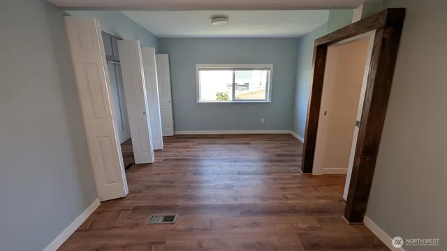 an empty room with wooden floor mirror and windows