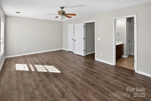 a view of an empty room with wooden floor and a ceiling fan