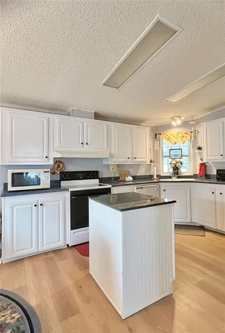 a kitchen with stainless steel appliances granite countertop a stove top oven a sink a refrigerator white cabinets and a wooden floor