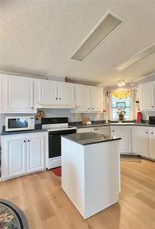 a kitchen with stainless steel appliances granite countertop a stove top oven a sink a refrigerator white cabinets and a wooden floor