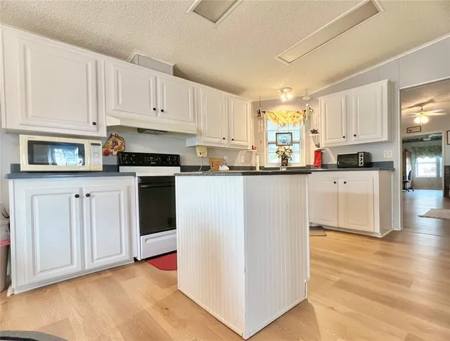 a kitchen with stainless steel appliances granite countertop a stove top oven a sink a refrigerator white cabinets and wooden floor