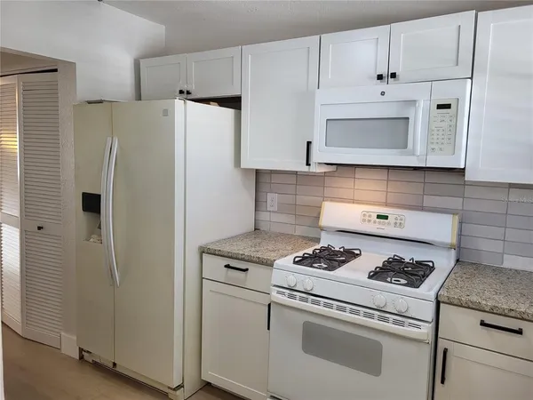 a white refrigerator freezer and a stove sitting inside of a kitchen with granite countertop cabinets