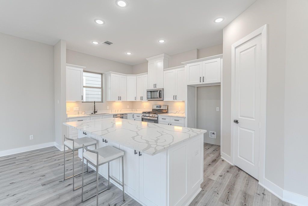 15038 Wunderlust Houston, TX 77069 - Photo 3 of 27 a large kitchen with kitchen island a stove a sink a refrigerator and white cabinets with wooden floor