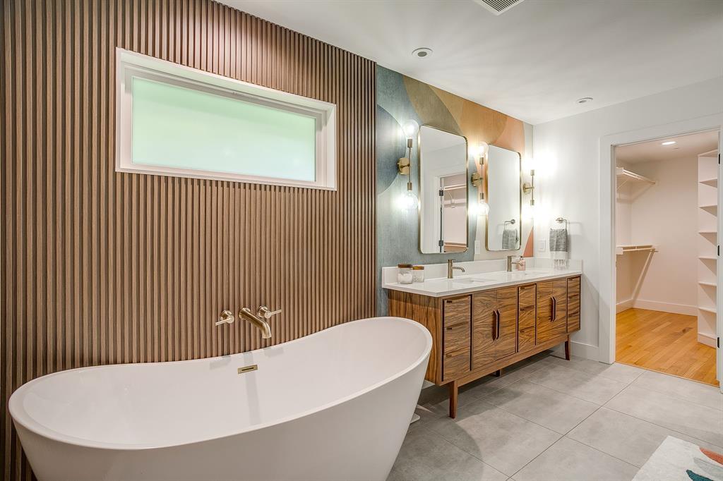 6700 Fortune Road Fort Worth, TX 76116 - Photo 25 of 40 Bathroom featuring a freestanding soaking tub with wall-mounted brass fixtures, a wood-finish double vanity with dual rectangular mirrors and sconce lighting, and a walk-in closet with built-in shelving