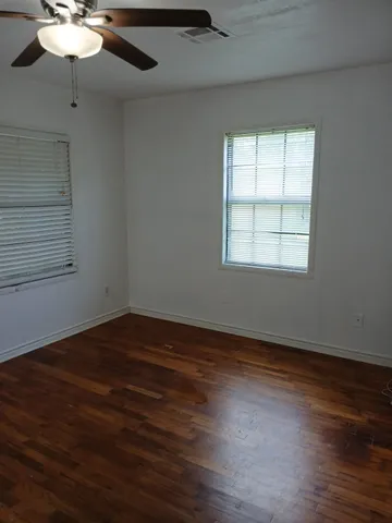 an empty room with wooden floor chandelier fan and windows
