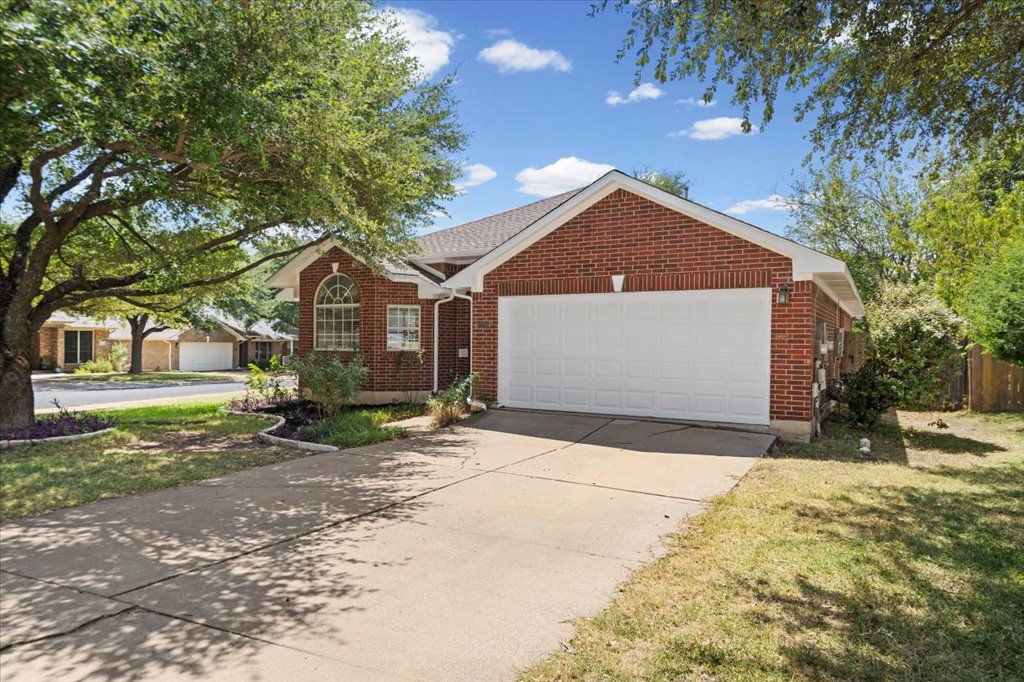 13200 Calf Roping Trail Austin, TX 78727 - Photo 27 of 28 Mature trees shade a classic brick facade featuring an attached garage and concrete driveway.